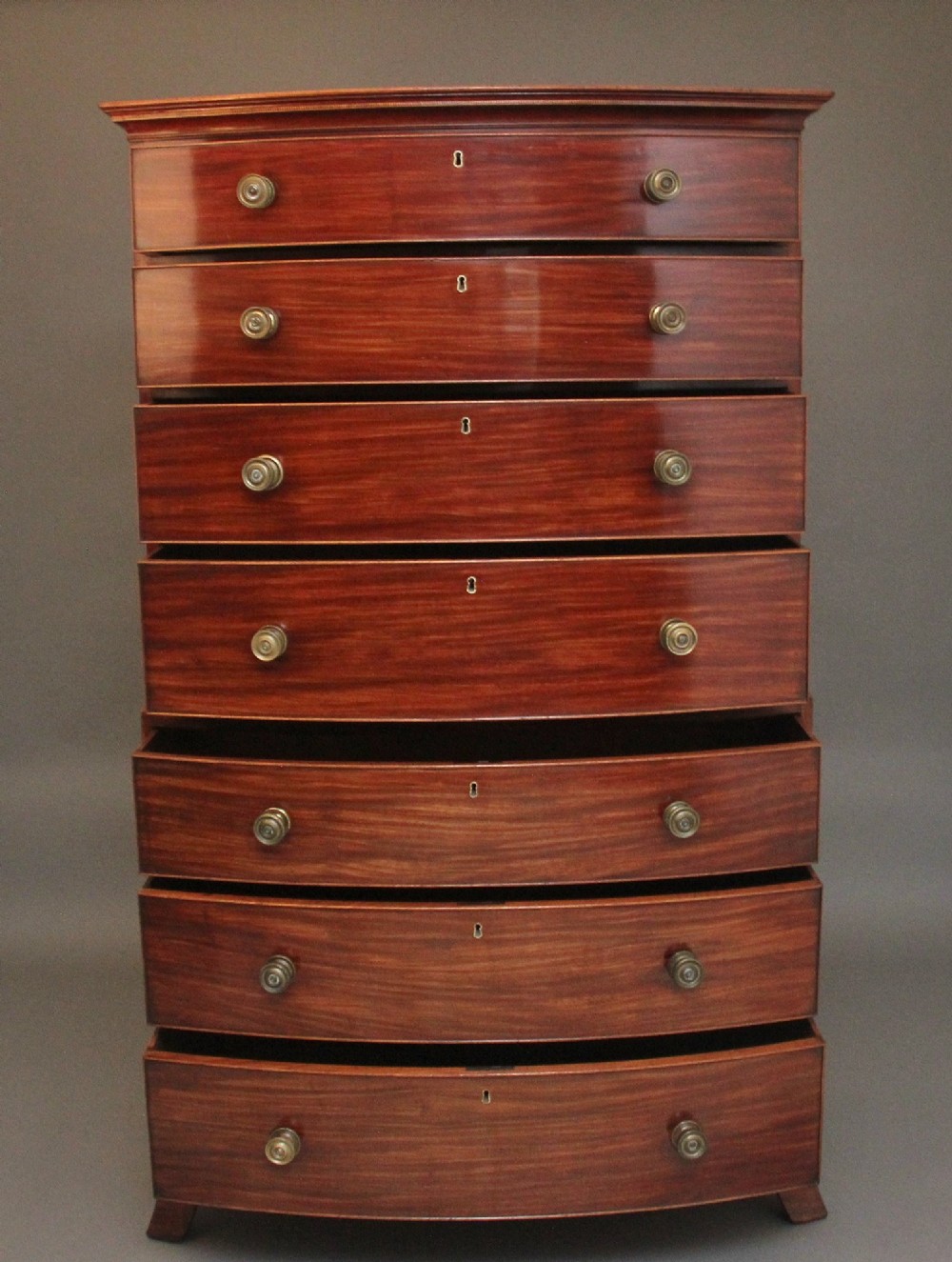An early nineteenth-century mahogany bow-front tallboy featuring seven stacked drawers with turned brass handles. View II
