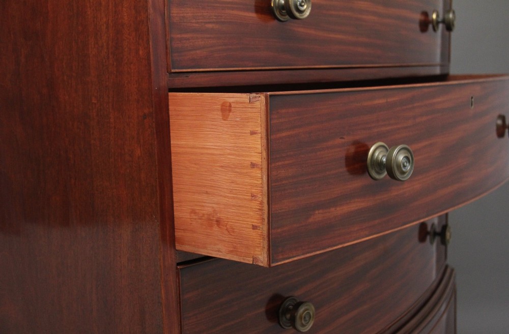 An early nineteenth-century mahogany bow-front tallboy featuring seven stacked drawers with turned brass handles. View IX
