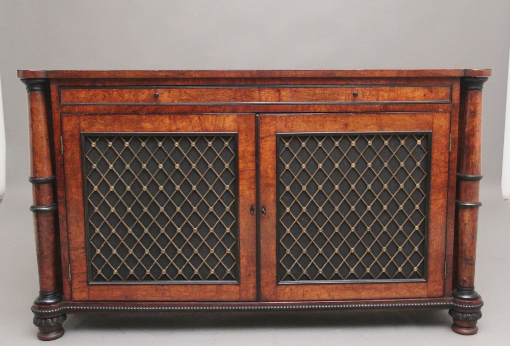An early nineteenth-century Regency pollard oak side cabinet featuring ebony inlay, twin brass lattice grille doors with fabric backings, and side columns.