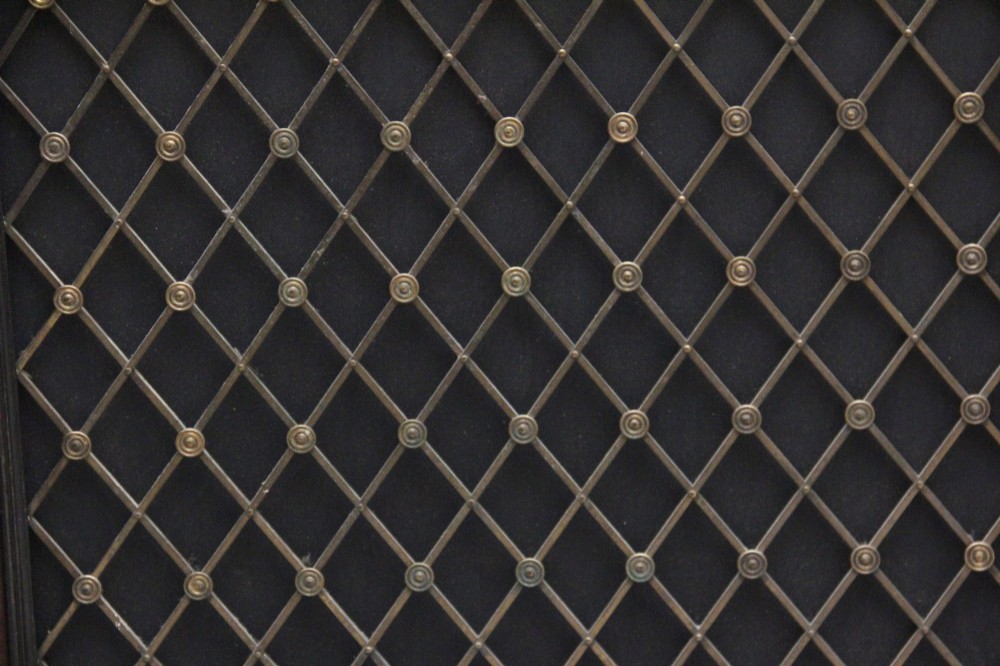 An early nineteenth-century Regency pollard oak side cabinet featuring ebony inlay, twin brass lattice grille doors with fabric backings, and side columns. View XV