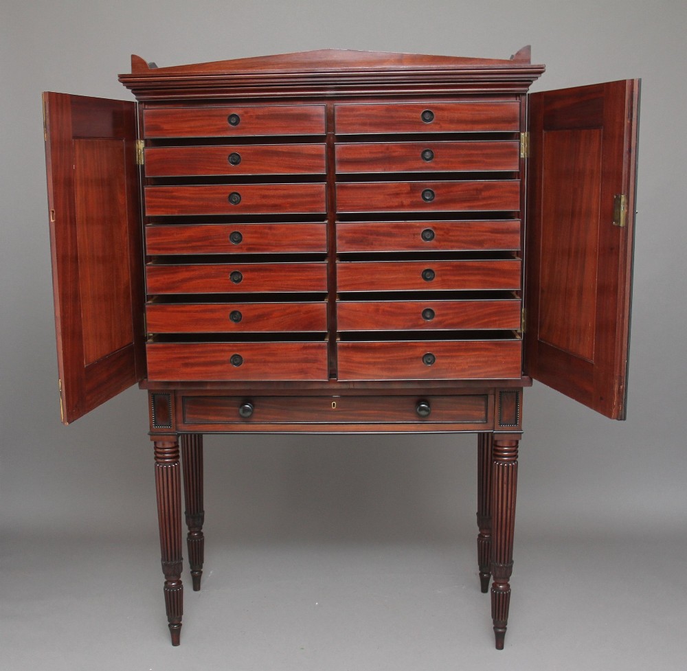 An early 19th-century mahogany collectors cabinet on stand featuring flame mahogany door panels, a single drawer, and four turned reeded legs. View V