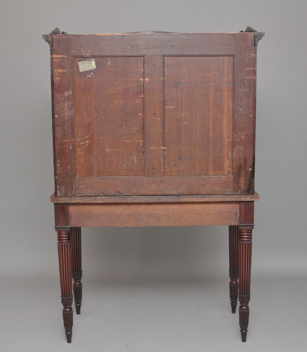 An early 19th-century mahogany collectors cabinet on stand featuring flame mahogany door panels, a single drawer, and four turned reeded legs. View VIII