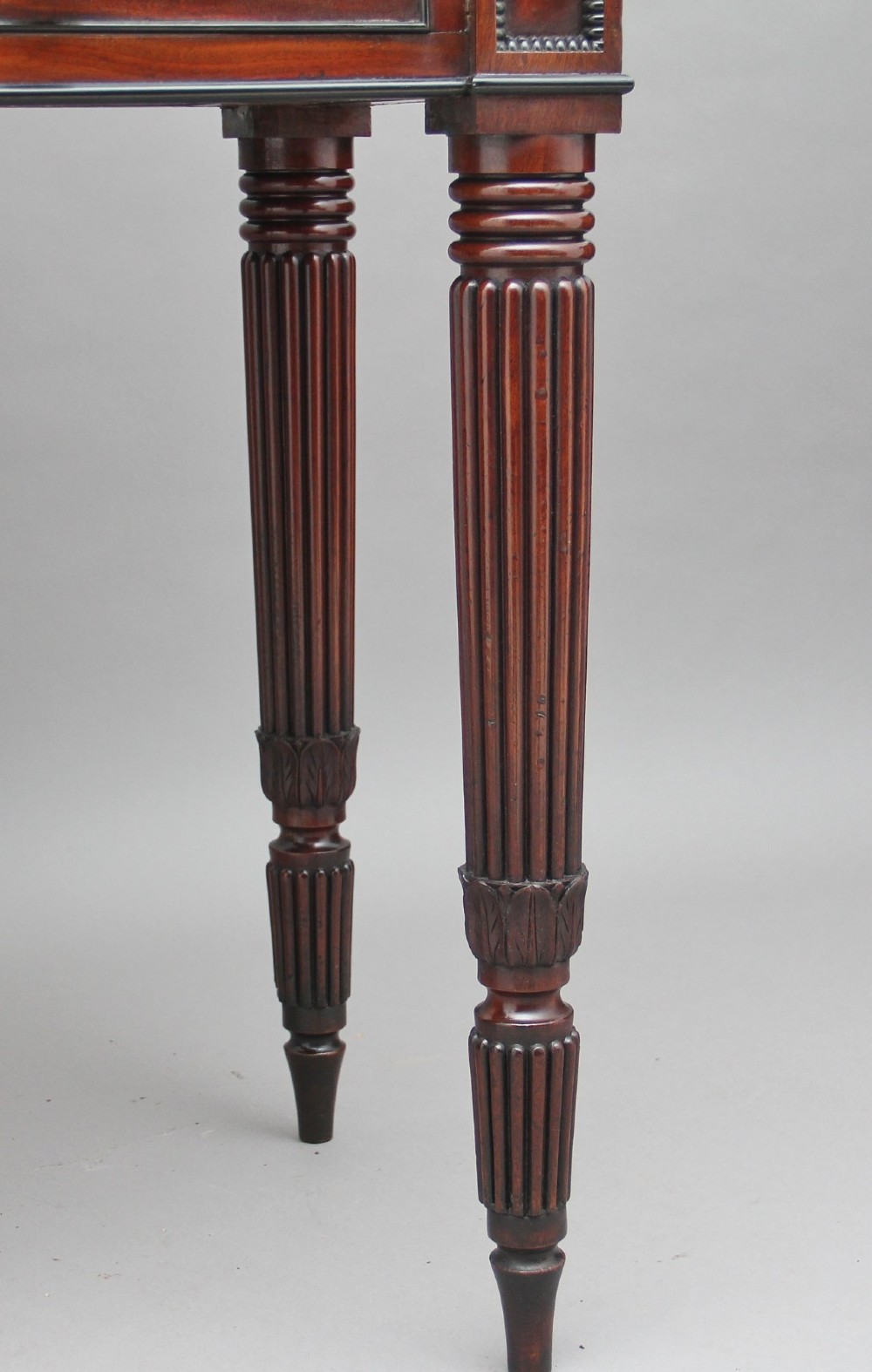 An early 19th-century mahogany collectors cabinet on stand featuring flame mahogany door panels, a single drawer, and four turned reeded legs. View XV