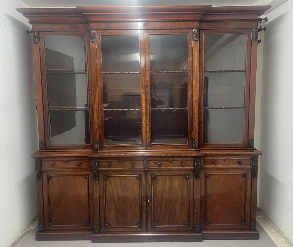 An early nineteenth-century mahogany breakfront bookcase featuring four glazed upper doors over four panelled lower cupboard doors.