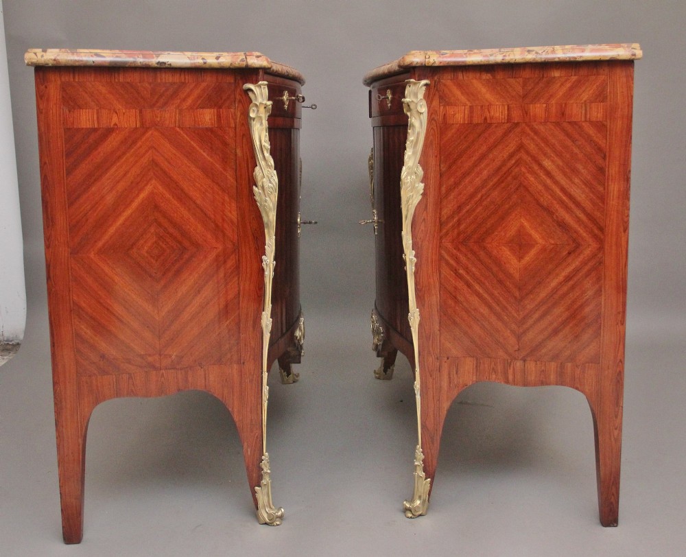 A pair of 19th-century French kingwood commodes featuring chevron parquetry veneer, mottled brown marble tops, and decorative gilt-bronze mounts. View V