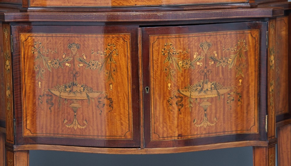 A 19th-century satinwood display cabinet featuring a swan-neck pediment, curved central glass door, and marquetry inlaid lower doors on square tapered legs. View XI