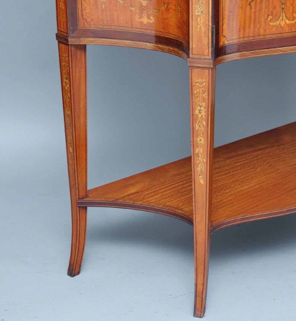 A 19th-century satinwood display cabinet featuring a swan-neck pediment, curved central glass door, and marquetry inlaid lower doors on square tapered legs. View XIV