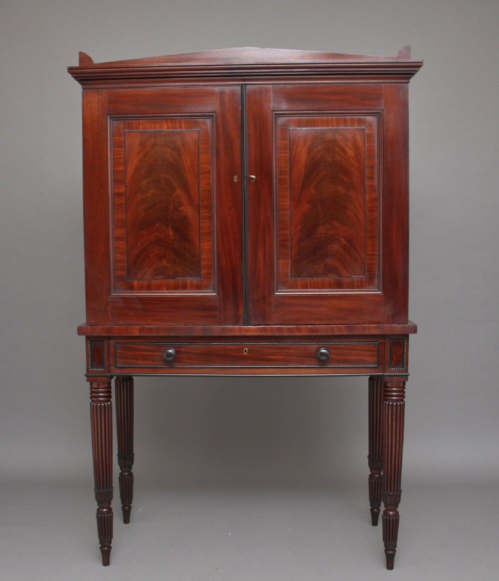 An early nineteenth-century flame mahogany collectors cabinet on stand featuring twin panelled doors above a single drawer and turned reeded legs.
