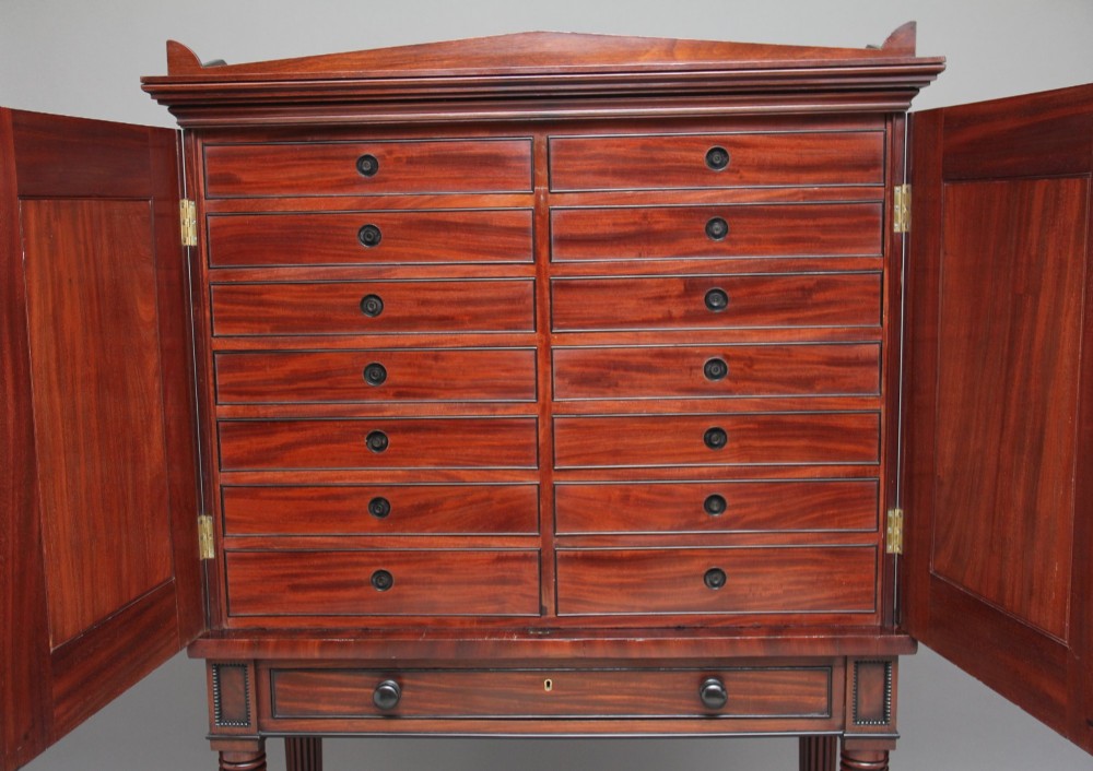 An early nineteenth-century flame mahogany collectors cabinet on stand featuring twin panelled doors above a single drawer and turned reeded legs. View XI