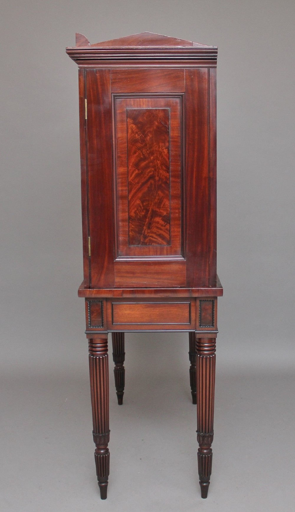 An early nineteenth-century flame mahogany collectors cabinet on stand featuring twin panelled doors above a single drawer and turned reeded legs. View XII