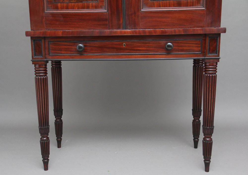 An early nineteenth-century flame mahogany collectors cabinet on stand featuring twin panelled doors above a single drawer and turned reeded legs. View XIII