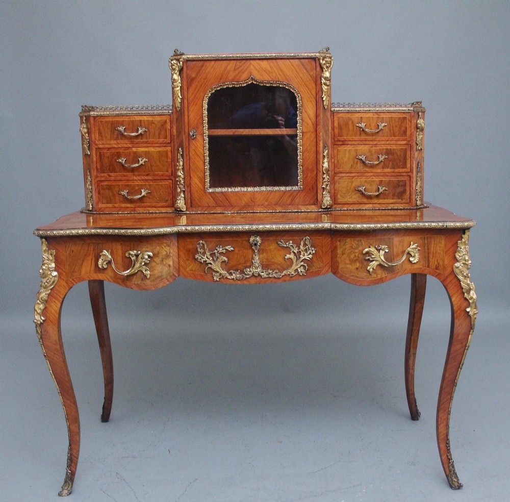A 19th-century walnut writing desk featuring a raised superstructure with a central glazed cupboard flanked by small drawers, trimmed with gilt-bronze mounts on cabriole legs.