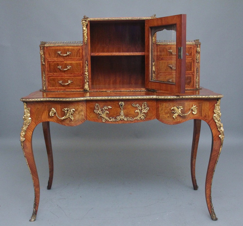 A 19th-century walnut writing desk featuring a raised superstructure with a central glazed cupboard flanked by small drawers, trimmed with gilt-bronze mounts on cabriole legs. View IV