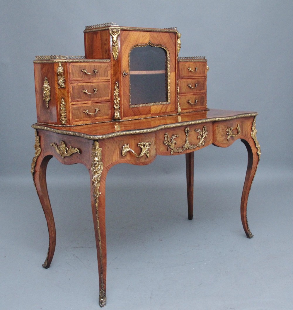 A 19th-century walnut writing desk featuring a raised superstructure with a central glazed cupboard flanked by small drawers, trimmed with gilt-bronze mounts on cabriole legs. View V