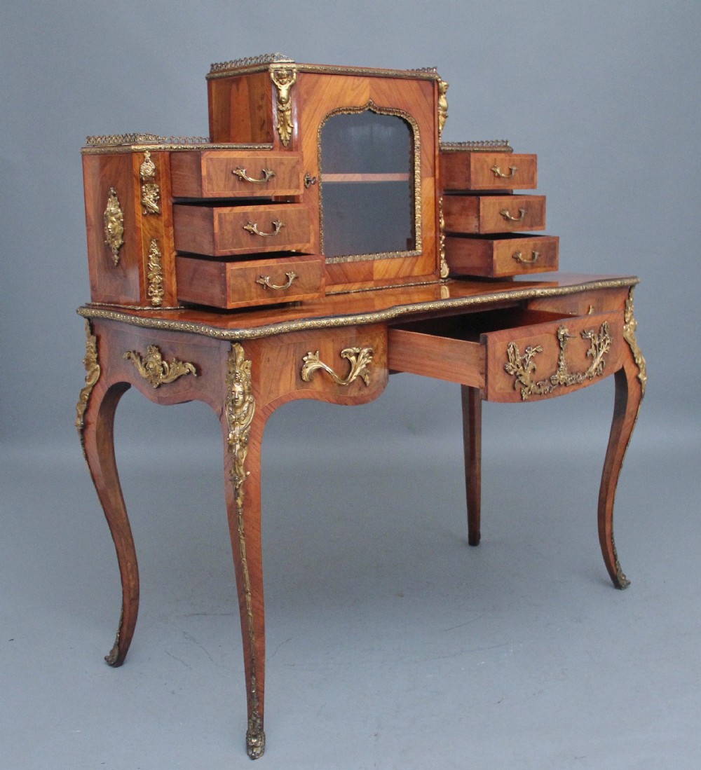 A 19th-century walnut writing desk featuring a raised superstructure with a central glazed cupboard flanked by small drawers, trimmed with gilt-bronze mounts on cabriole legs. View VI
