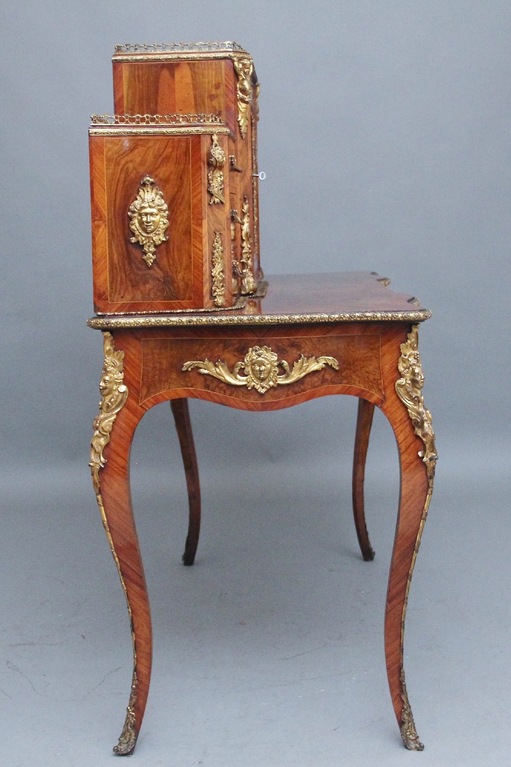 A 19th-century walnut writing desk featuring a raised superstructure with a central glazed cupboard flanked by small drawers, trimmed with gilt-bronze mounts on cabriole legs. View VII