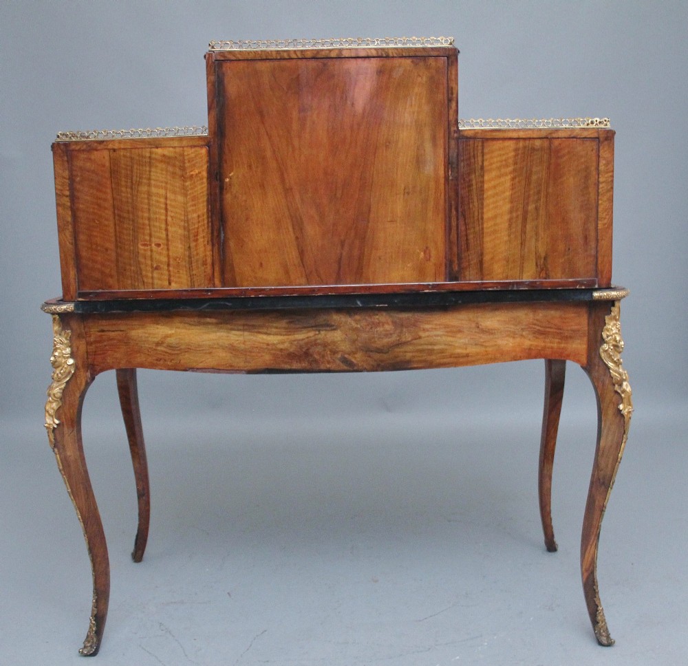 A 19th-century walnut writing desk featuring a raised superstructure with a central glazed cupboard flanked by small drawers, trimmed with gilt-bronze mounts on cabriole legs. View X