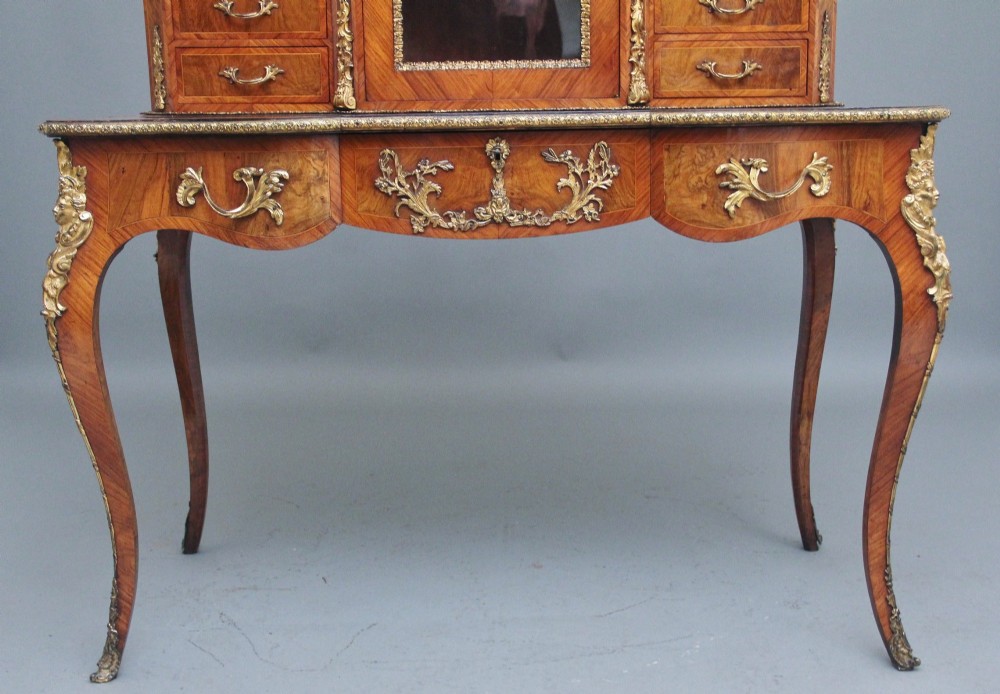 A 19th-century walnut writing desk featuring a raised superstructure with a central glazed cupboard flanked by small drawers, trimmed with gilt-bronze mounts on cabriole legs. View XII