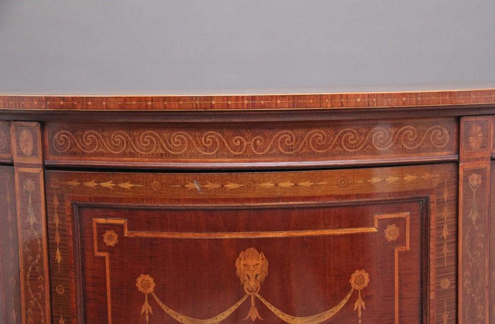 A 19th-century bow-fronted mahogany side cabinet featuring detailed satinwood marquetry panels with classical figures and swags on turned tapered legs. View IX