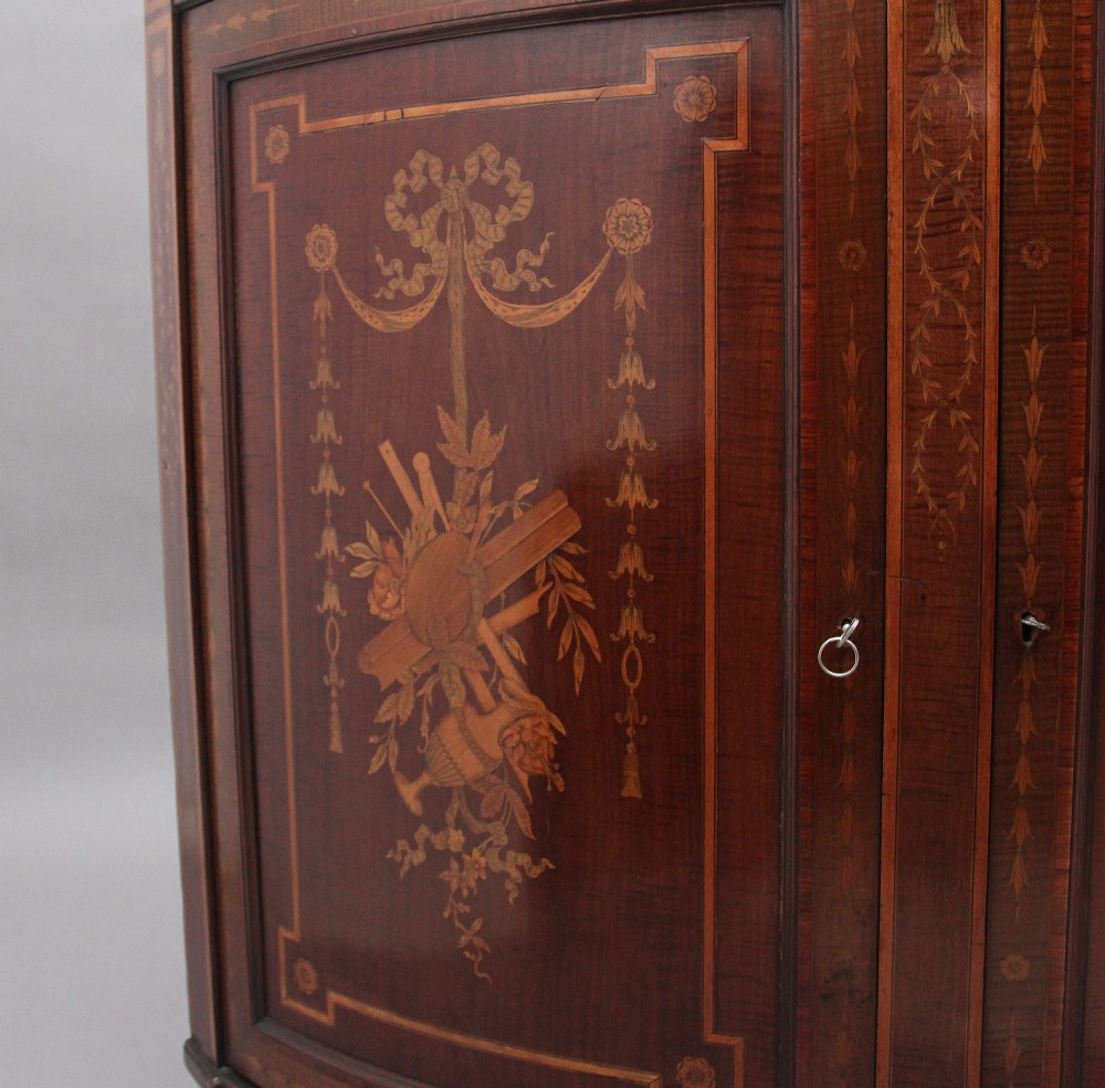 A 19th-century bow-fronted mahogany side cabinet featuring detailed satinwood marquetry panels with classical figures and swags on turned tapered legs. View XIII