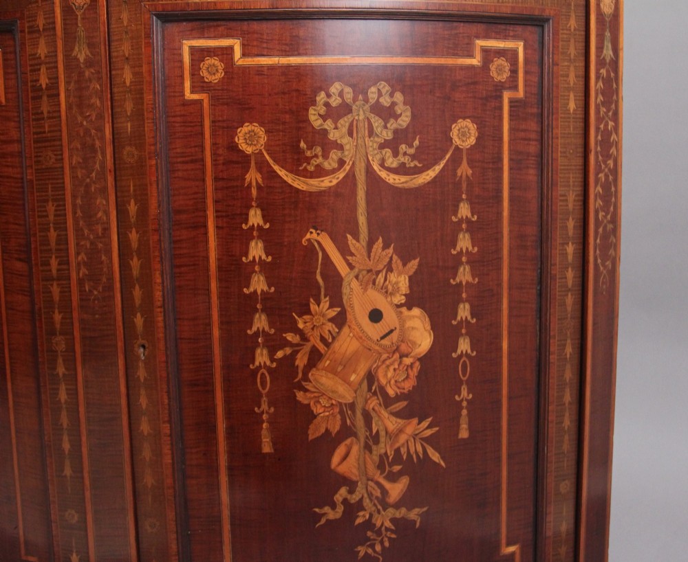 A 19th-century bow-fronted mahogany side cabinet featuring detailed satinwood marquetry panels with classical figures and swags on turned tapered legs. View XIV