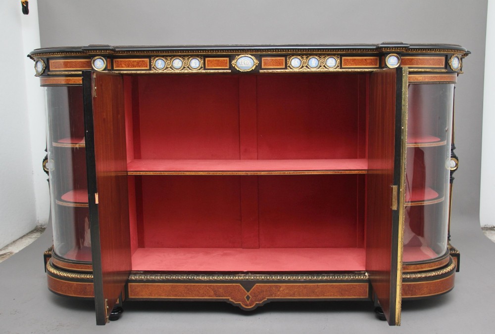 A 19th-century Victorian amboyna and ebonised credenza featuring curved glass side cabinets, gilt-metal mounts, porcelain plaque frieze details, and central oval panels inlaid with stone floral motifs. View III