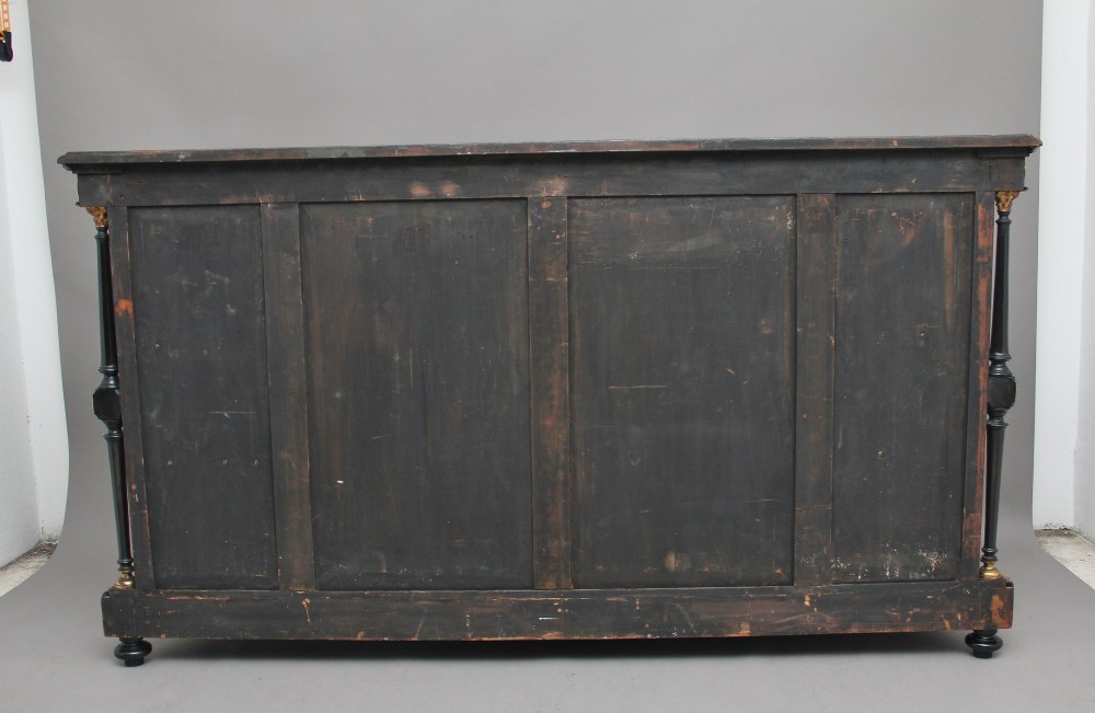 A 19th-century Victorian amboyna and ebonised credenza featuring curved glass side cabinets, gilt-metal mounts, porcelain plaque frieze details, and central oval panels inlaid with stone floral motifs. View VI