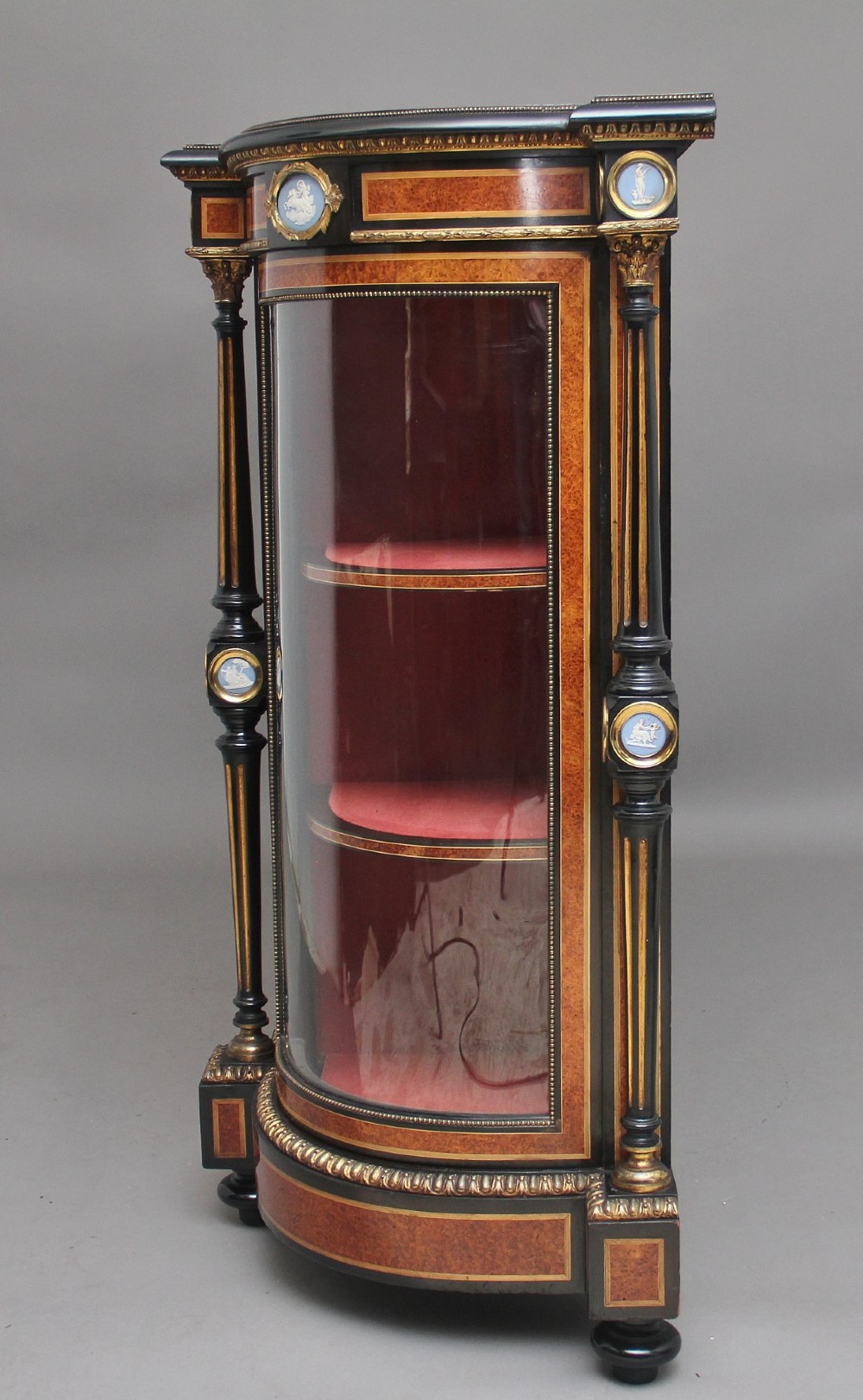 A 19th-century Victorian amboyna and ebonised credenza featuring curved glass side cabinets, gilt-metal mounts, porcelain plaque frieze details, and central oval panels inlaid with stone floral motifs. View VII