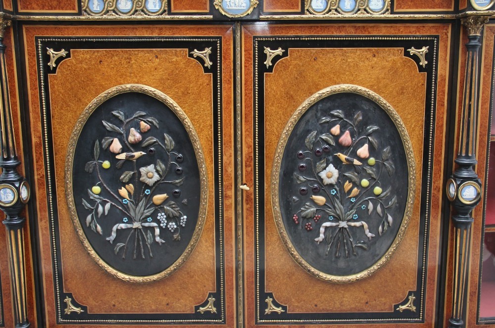A 19th-century Victorian amboyna and ebonised credenza featuring curved glass side cabinets, gilt-metal mounts, porcelain plaque frieze details, and central oval panels inlaid with stone floral motifs. View VIII