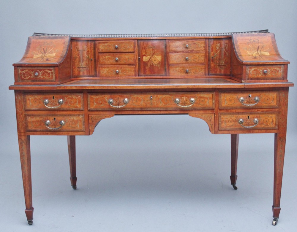 A 19th-century satinwood Carlton House desk featuring floral marquetry inlay, multiple small drawers, a central writing surface, a brass gallery rail, and square tapered legs on castors.