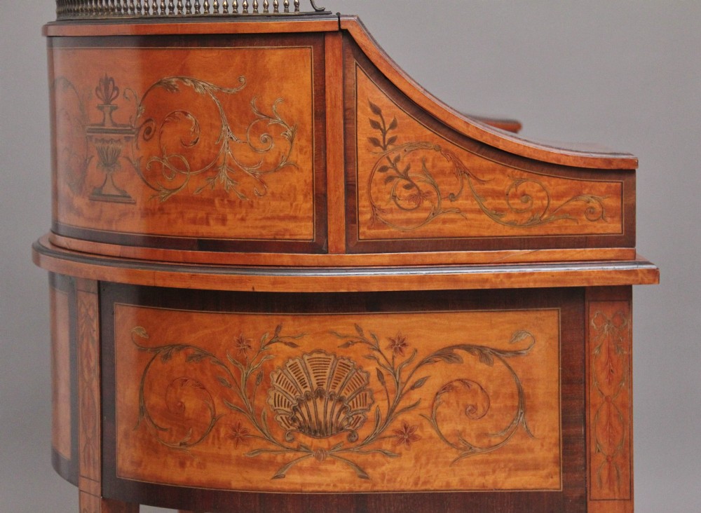 A 19th-century satinwood Carlton House desk featuring floral marquetry inlay, multiple small drawers, a central writing surface, a brass gallery rail, and square tapered legs on castors. View VII