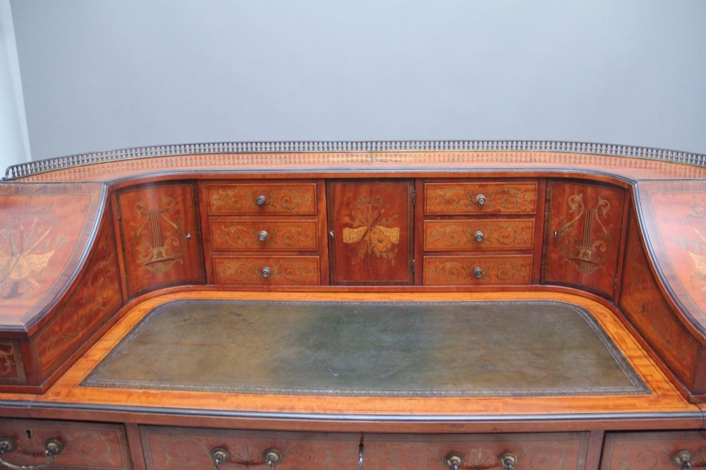 A 19th-century satinwood Carlton House desk featuring floral marquetry inlay, multiple small drawers, a central writing surface, a brass gallery rail, and square tapered legs on castors. View XI
