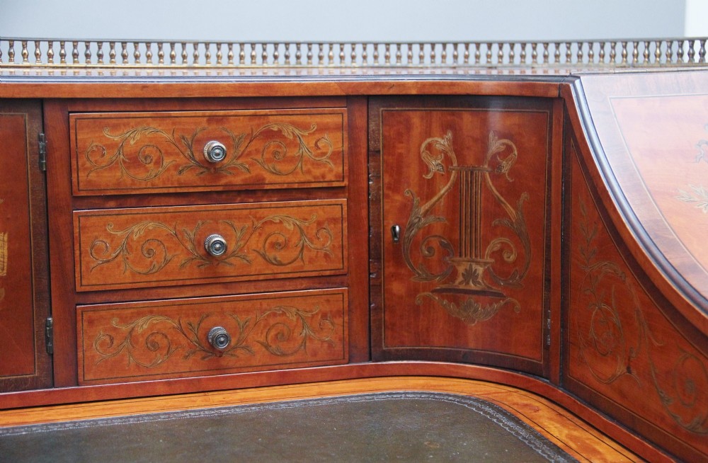 A 19th-century satinwood Carlton House desk featuring floral marquetry inlay, multiple small drawers, a central writing surface, a brass gallery rail, and square tapered legs on castors. View XIV