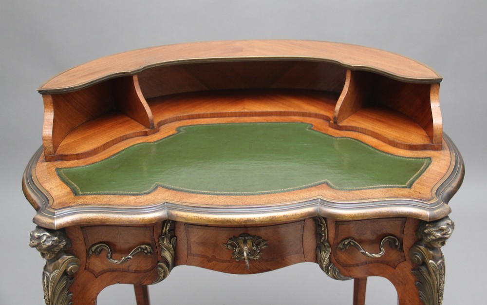 A 19th-century kingwood writing table featuring decorative gilt-bronze ormolu mounts, cabriole legs, a green leather writing surface, and a raised superstructure with pigeonholes. View V