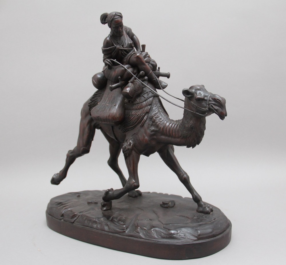 A nineteenth-century dark carved wood sculpture depicting a figure in flowing robes riding a trotting camel mounted on an oval base.