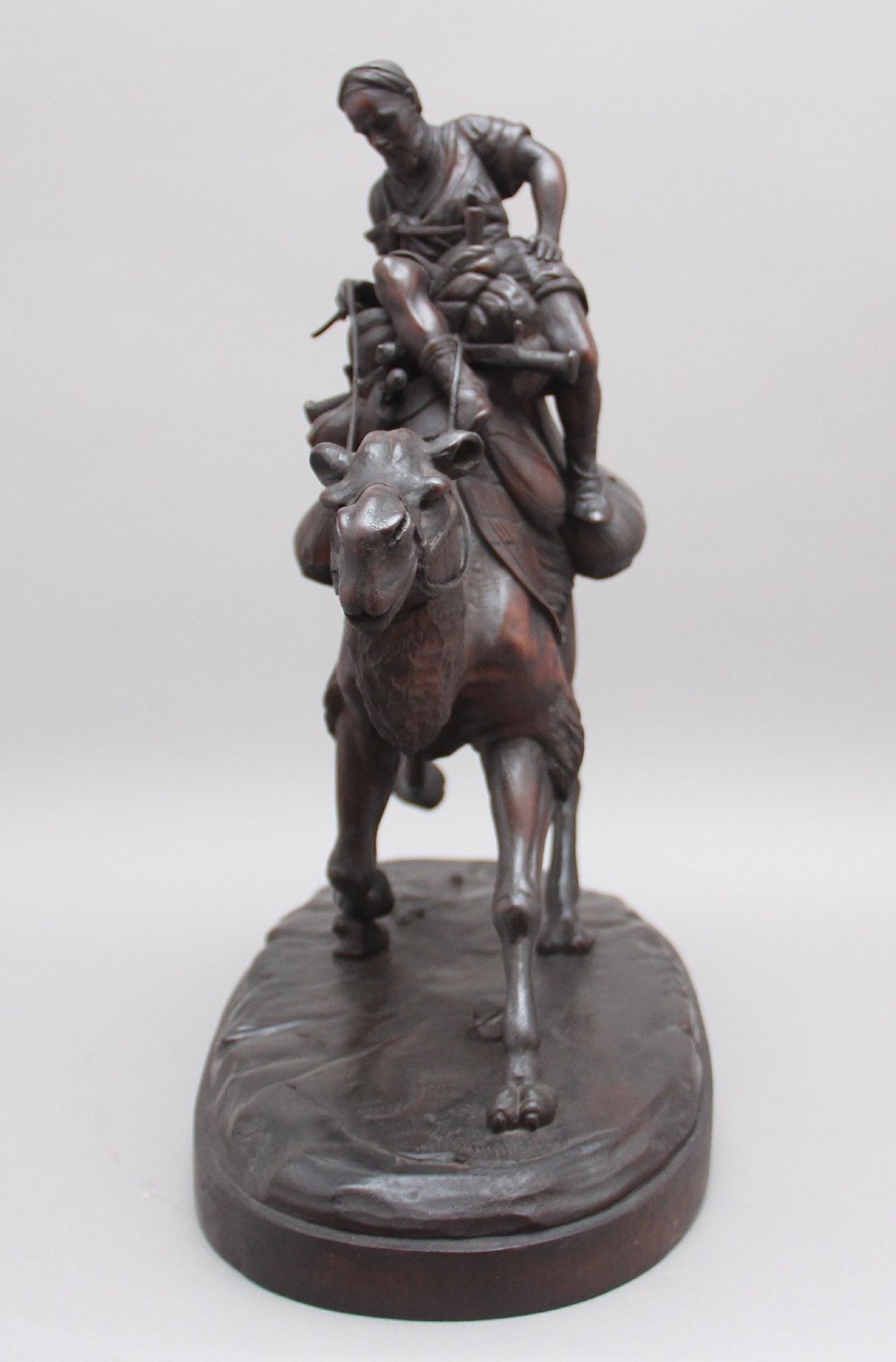 A nineteenth-century dark carved wood sculpture depicting a figure in flowing robes riding a trotting camel mounted on an oval base. View III