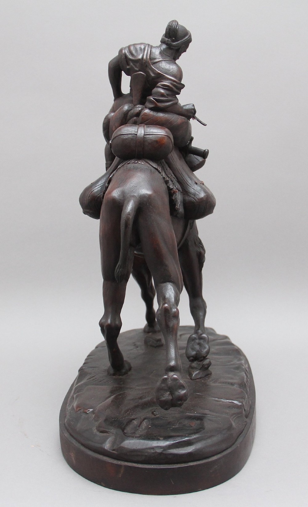 A nineteenth-century dark carved wood sculpture depicting a figure in flowing robes riding a trotting camel mounted on an oval base. View V