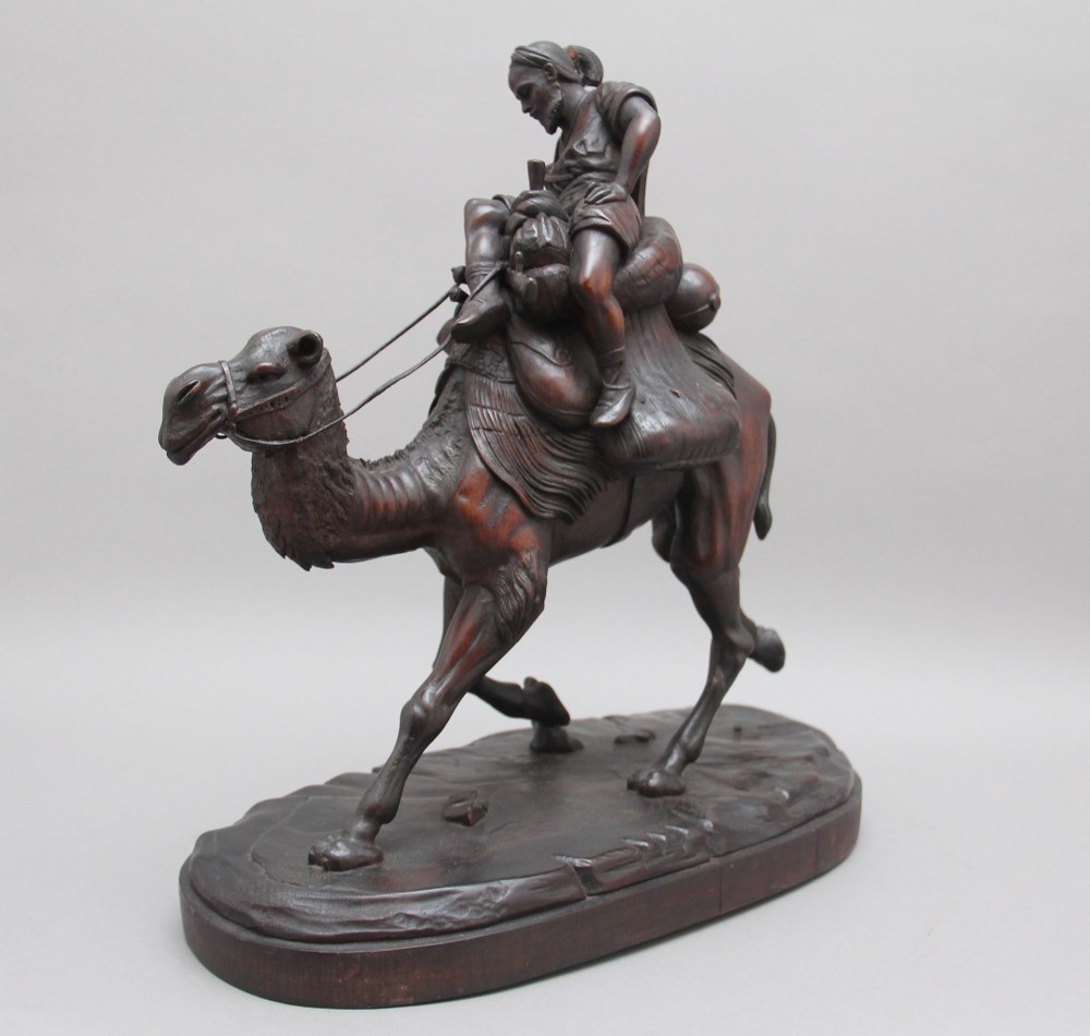 A nineteenth-century dark carved wood sculpture depicting a figure in flowing robes riding a trotting camel mounted on an oval base. View VI