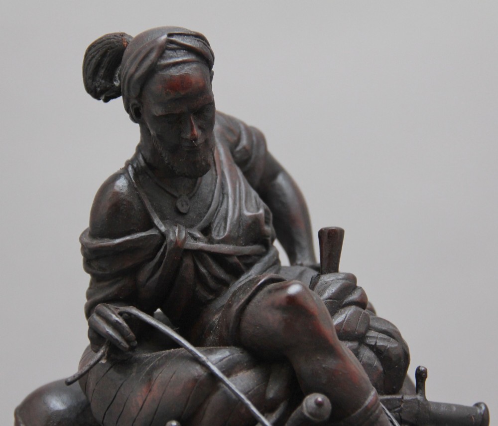 A nineteenth-century dark carved wood sculpture depicting a figure in flowing robes riding a trotting camel mounted on an oval base. View IX