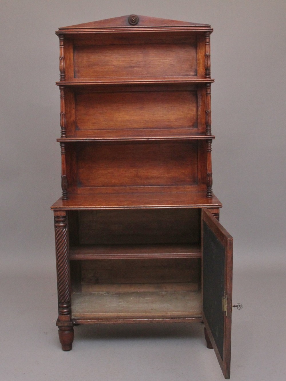 An early nineteenth-century oak bookcase featuring three open upper shelves, a pediment top, and a lower cabinet with a brass wire mesh door flanked by rope-twist columns. View III