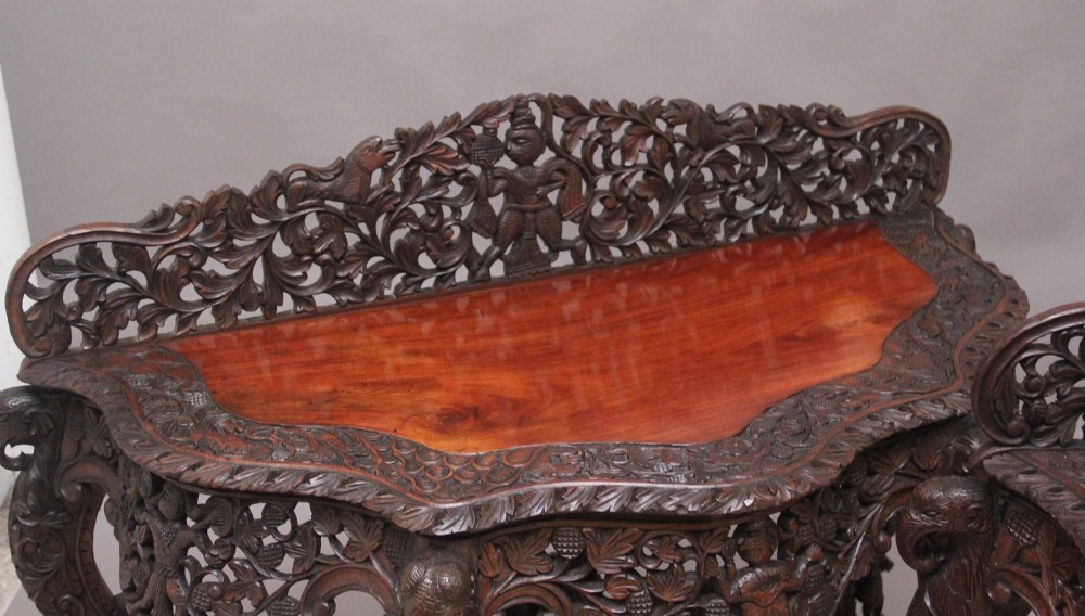 A pair of 19th-century dark wood console tables featuring intricate openwork carving, gallery backs, curved legs, and polished timber tops. View V