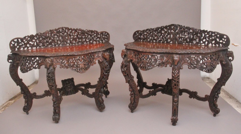 A pair of 19th-century dark wood console tables featuring intricate openwork carving, gallery backs, curved legs, and polished timber tops. View X