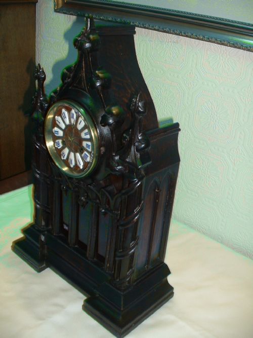 fig 1. A dark carved wooden bracket clock featuring Gothic architectural arches, decorative spires, twist columns, and a brass dial with white enamel hour markers.