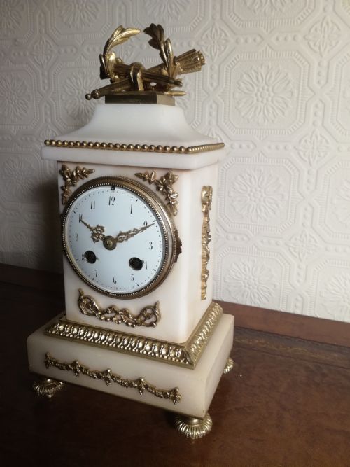 fig 1. A French Louis XVI style white marble mantel clock featuring gilt bronze mounts, a laurel wreath finial, and an enamel dial.