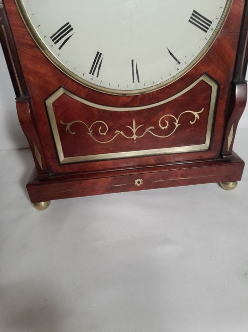 fig 1. A Georgian mahogany bracket clock featuring brass inlay decoration, carved foliage cresting, and a white circular dial with Roman numerals.