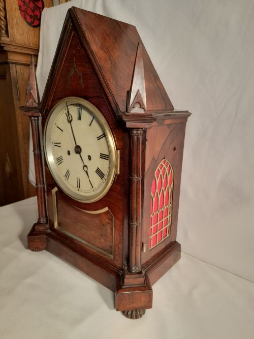 fig 1. An antique Gothic Revival rosewood bracket clock with pointed arch pinnacles, brass foliate inlay, and a circular white dial with Roman numerals.