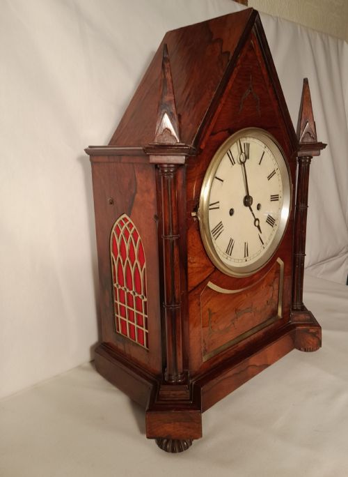 fig 2. An antique Gothic Revival rosewood bracket clock with pointed arch pinnacles, brass foliate inlay, and a circular white dial with Roman numerals.