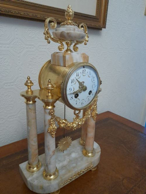 fig 1. A French Louis XVI style marble and gilt brass portico mantel clock featuring four columns, floral swags, an urn finial, and an enamel dial.