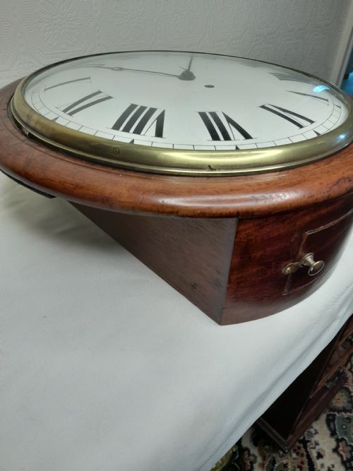 fig 2. An antique circular mahogany wall clock featuring a cream convex dial with black Roman numerals and a polished brass bezel.
