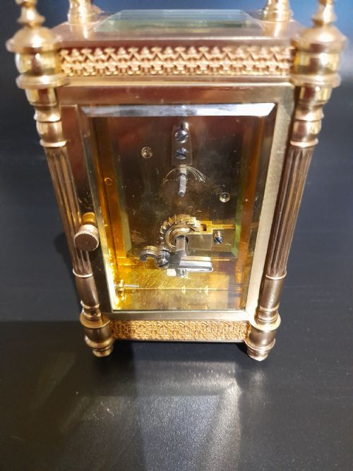 fig 1. A gilded brass carriage clock featuring clear glass side panels, turned corner columns, a folding top handle, and a white enamel dial with Arabic numerals.
